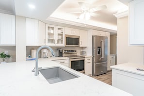 A modern kitchen with white cabinetry, stainless steel appliances, and a central island with a sink. - Sayana Unit 102 - Amazing Beachside Retreat (Sanibel)
