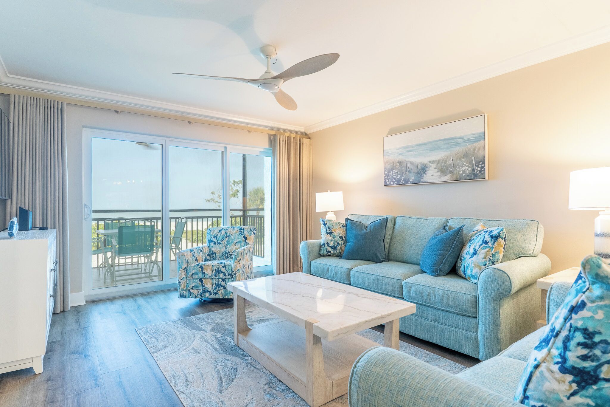 A spacious living room with a ceiling fan, a sofa set, a coffee table, and a painting on the wall.