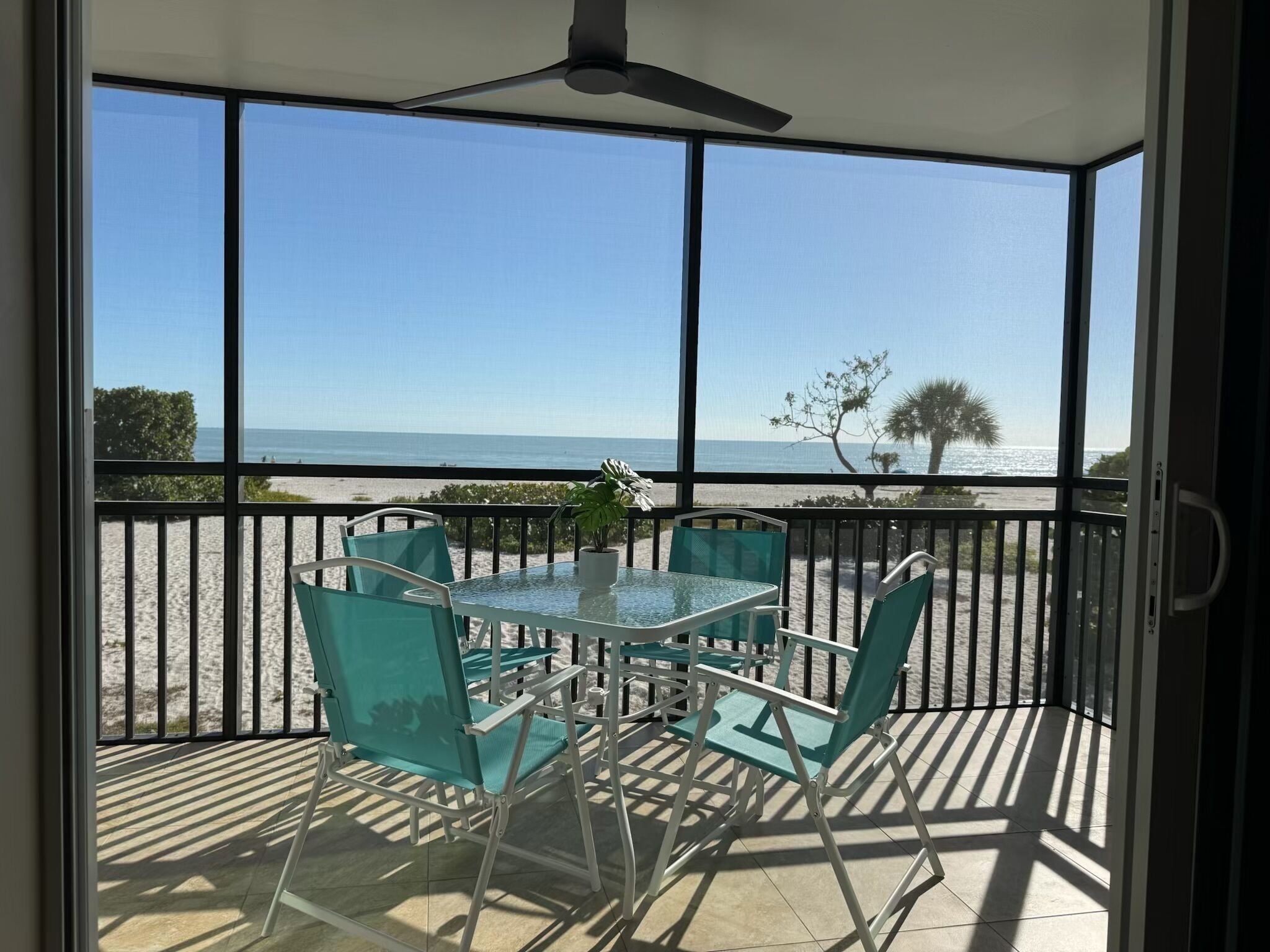 A balcony with a glass table and chairs, overlooking a beach.