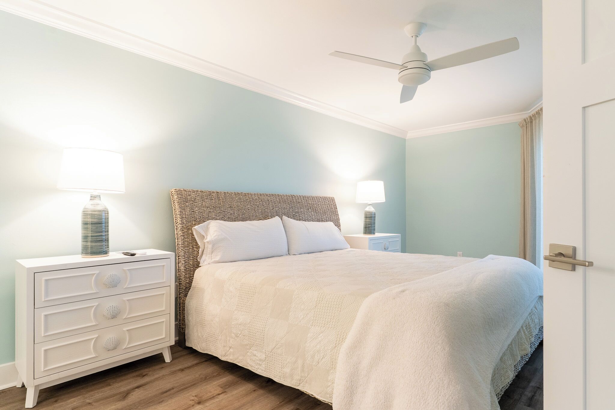 A bedroom with a bed, nightstands, a ceiling fan, and a door.