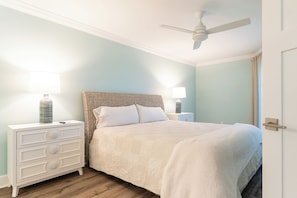A bedroom with a bed, nightstands, a ceiling fan, and a door. - Sayana Unit 102 - Amazing Beachside Retreat (Sanibel)