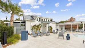 Un espace aménagé au bord de la piscine, avec des chaises longues, un coin salon abrité et un bâtiment comprenant un garage.