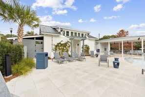 Ein Poolbereich mit Liegestühlen, einer überdachten Sitzgelegenheit und einem Gebäude mit Garage.