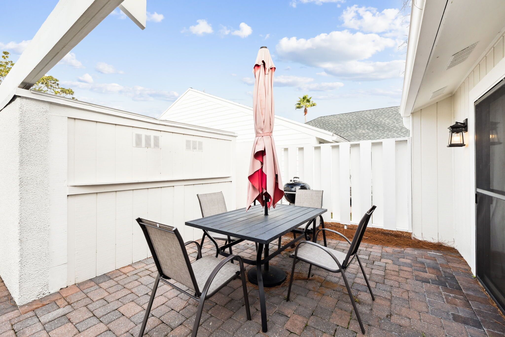 A patio with a table and chairs, a grill, and a white fence.