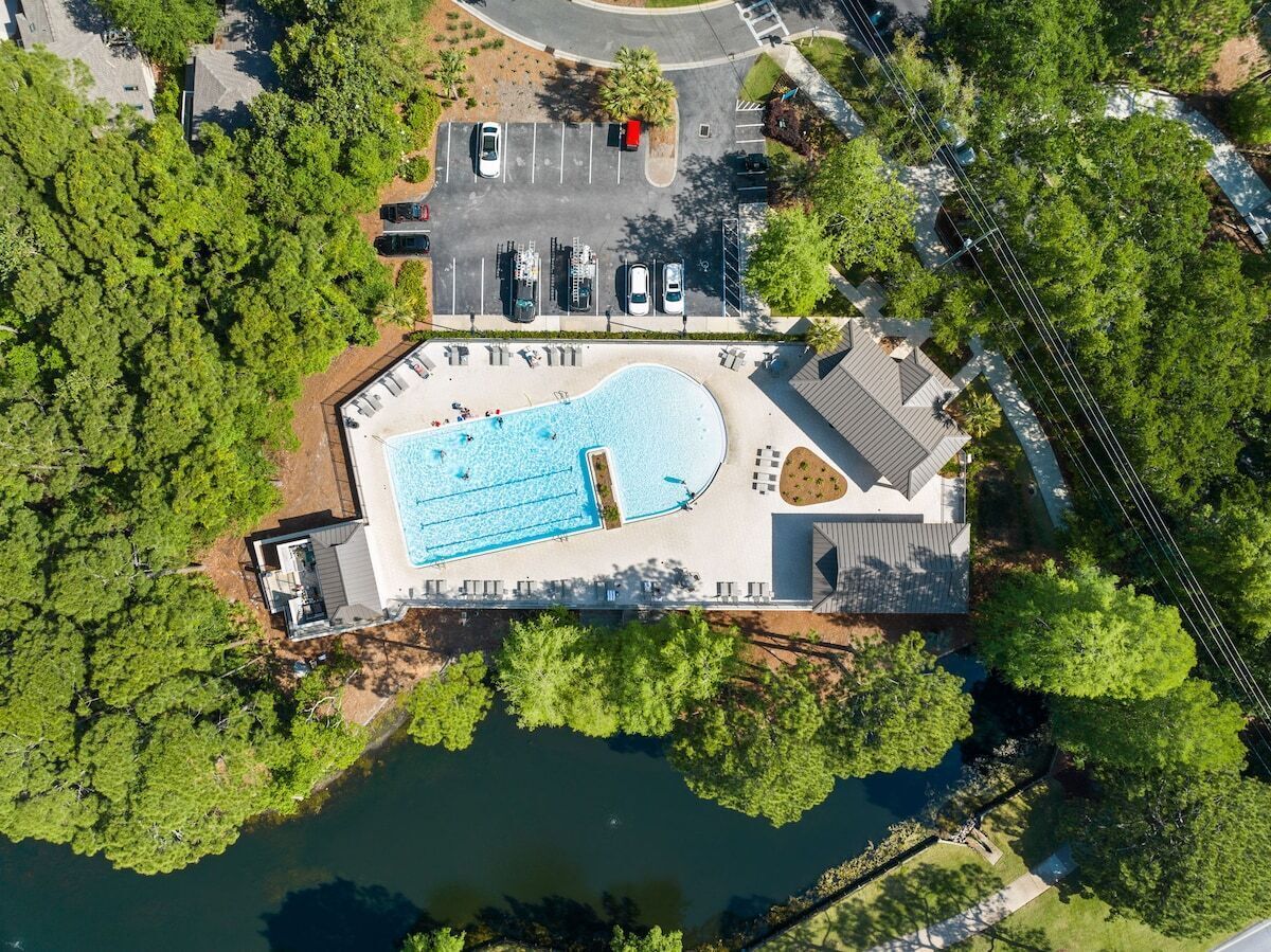 An aerial view of a property with a swimming pool, parking area, and surrounding greenery.
