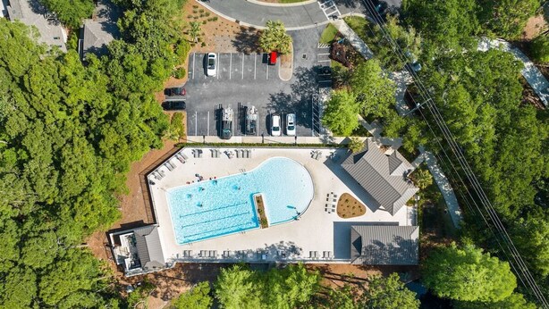 Vue aérienne d’une propriété dotée d’une piscine, d’un espace de stationnement et d’un espace vert environnant.