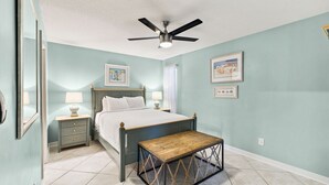 Une chambre à coucher avec un lit, des tables de chevet, un ventilateur de plafond et des œuvres d’art accrochées aux murs.