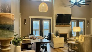A spacious living room with a fireplace, a television mounted on the wall, and a ceiling fan.