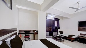 Habitación de hotel con cama, escritorio, silla, televisor y ventilador de techo.