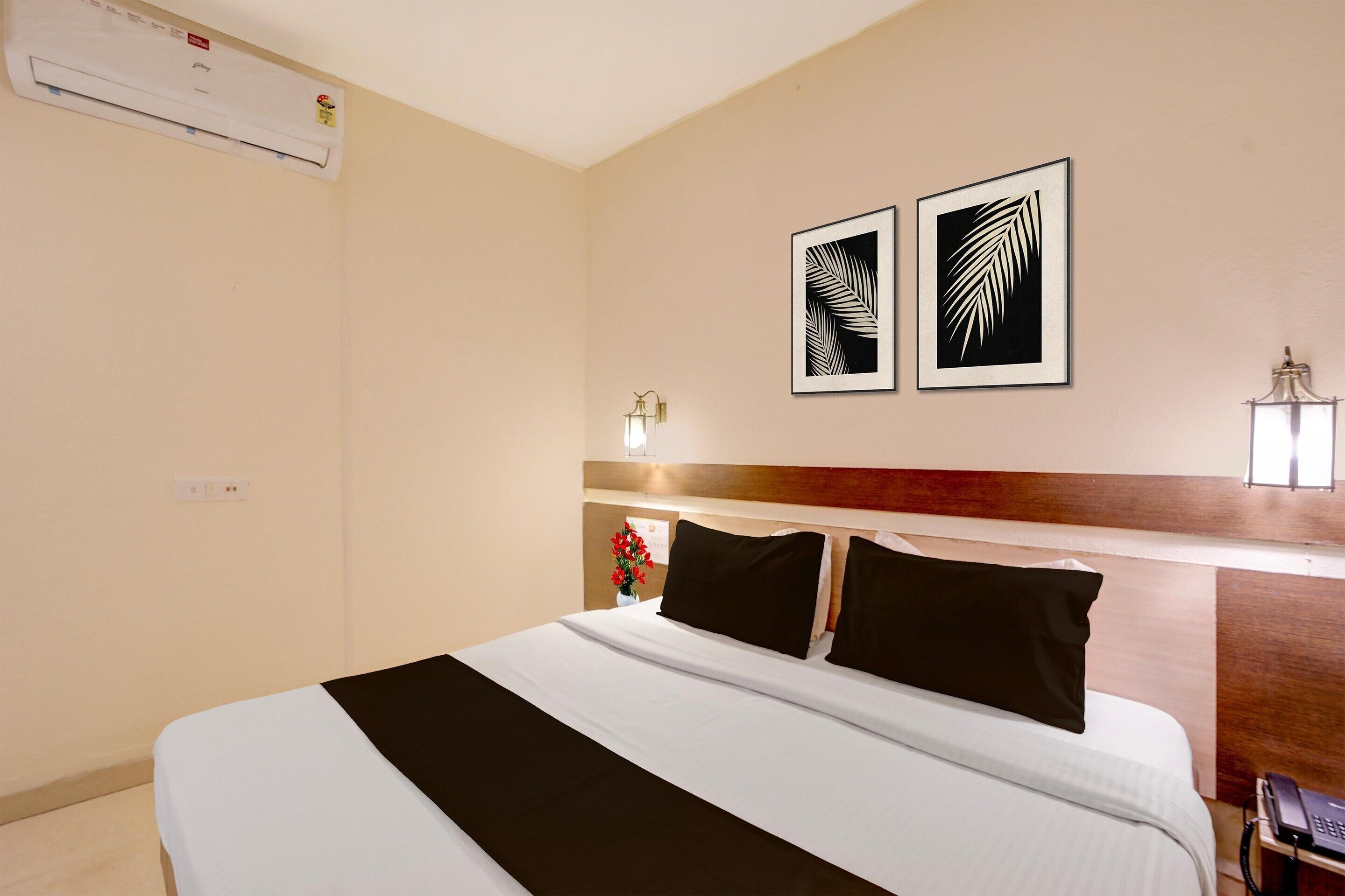 Habitació d'hotel amb llit, aire condicionat, obra penjada a la paret, làmpada de nit i un telèfon sobre un suport.