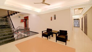Un vestíbulo de hotel con una escalera, un ventilador de techo, una zona de estar con dos sillas y una mesa, y una pared decorativa.