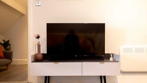 En moderne stue med et fladskærms-TV på et hvidt skab, en potteplante og en vase med en enkelt blomst.