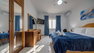 Habitación de hotel con cama, escritorio, espejo, armario, televisor y ventana con cortinas.