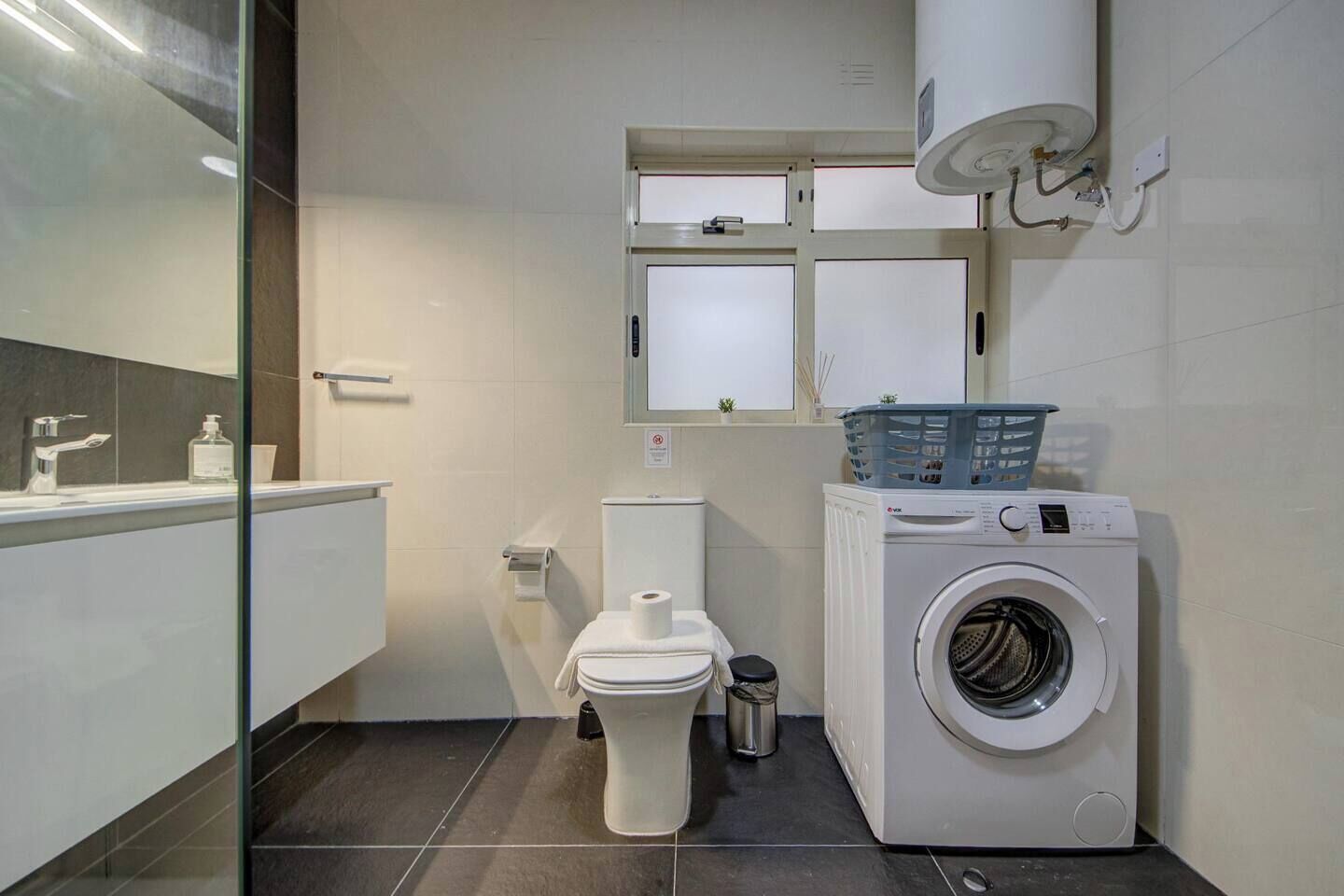 A compact bathroom with a toilet, washing machine, and a glass shower enclosure.