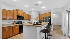 A modern kitchen with wooden cabinets, a central island with bar stools, stainless steel appliances, and recessed ceiling lights. - Luxury Hot Tub Getaway in Estrella Mountain Ranch (Goodyear)