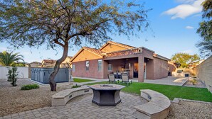 A residential backyard with a patio, outdoor seating, and a well-maintained lawn. - Luxury Hot Tub Getaway in Estrella Mountain Ranch (Goodyear)