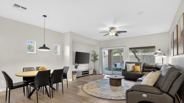A modern living room with a dining area, a sofa, a TV, and a ceiling fan. - Luxury Hot Tub Getaway in Estrella Mountain Ranch (Goodyear)