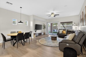 A modern living room with a dining area, a sofa, a TV, and a ceiling fan.