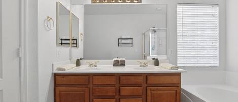 Une salle de bain avec un meuble-lavabo en bois, deux vasques, un grand miroir et une baignoire.