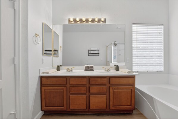 A bathroom with a wooden vanity, two sinks, a large mirror, and a bathtub.