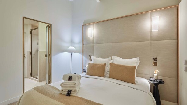 A modern hotel room with a large bed, a bedside table with a lamp, a mirror, and a door leading to a bathroom. - Exceptional Grand Apartment - Louvre Museum (Paris)