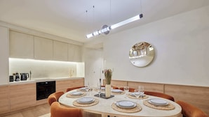 A modern dining area with a round table set for six, surrounded by orange chairs. - Exceptional Grand Apartment - Louvre Museum (Paris)