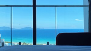 Habitación de hotel con un amplio ventanal que ofrece vistas al océano y montañas a lo lejos.