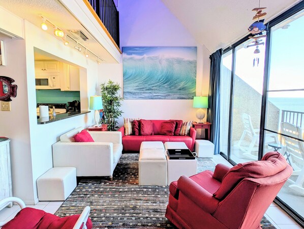 A modern living room with a red sofa, white armchairs, and a coffee table. A large window offers a view of the ocean. - 908 Dover - Sea Colony East (Bethany Beach)