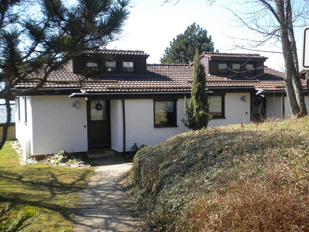 Une maison à deux étages, avec un toit en tuiles, une porte d’entrée et un petit porche.