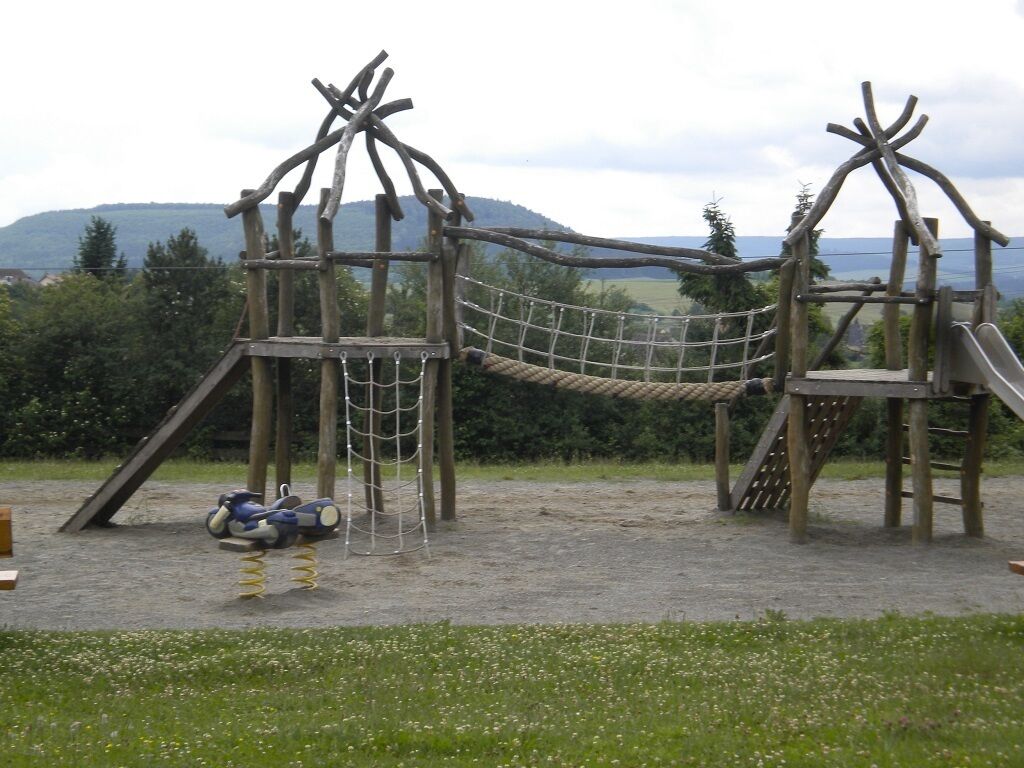 Une structure de jeux en bois comprenant un pont de corde, des toboggans et des éléments d’escalade.