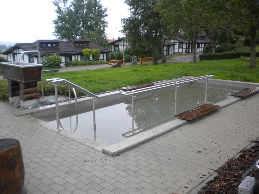 Une piscine équipée d’un escalier et de marches en métal, entourée d’une zone pavée avec des bancs et une structure en bois.