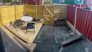 Eine Terrasse mit rundem Tisch, zwei Stühlen, einem Holzzaun und einer roten Wand.