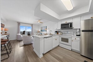 A modern kitchen with white cabinetry, a stainless steel refrigerator, and a built-in oven. - Seacrest 703 - 1 BR | Gulf Front | Sleeps 5 (Gulf Shores)