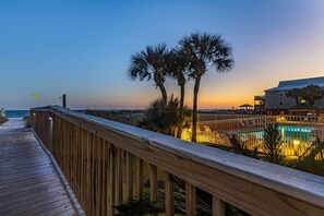 A wooden deck leading to a pool area with palm trees and a building in the background. - Seacrest 703 - 1 BR | Gulf Front | Sleeps 5 (Gulf Shores)