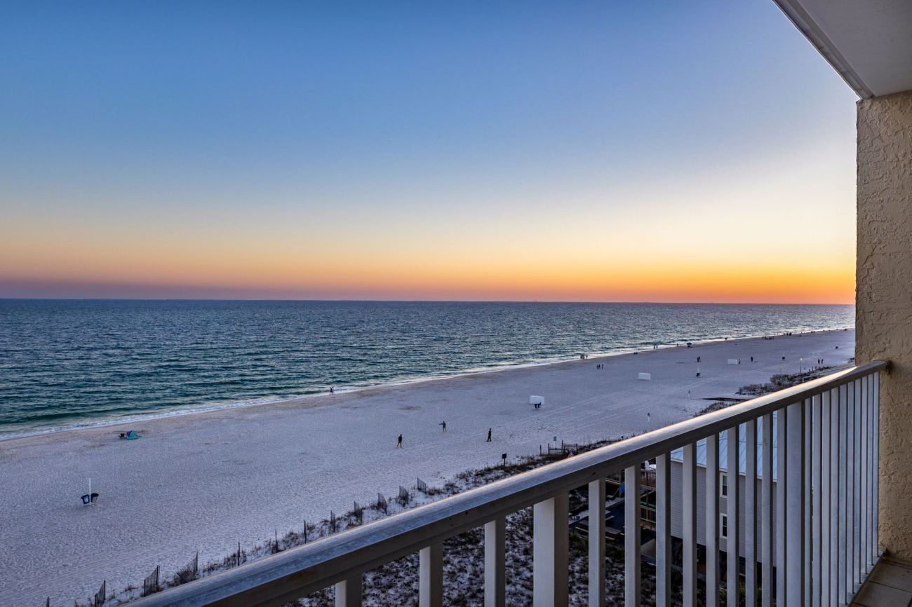 A beach view from a balcony with a railing, a clear sky, and the ocean.