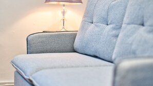 Et hjørne af et rum med en grå polstret lænestol og en bordlampe med lilla skærm.