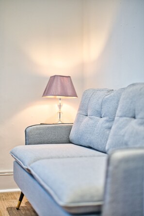 Eine Ecke eines Zimmers mit einem grau gepolsterten Sessel und einer Tischlampe mit einem violetten Lampenschirm.