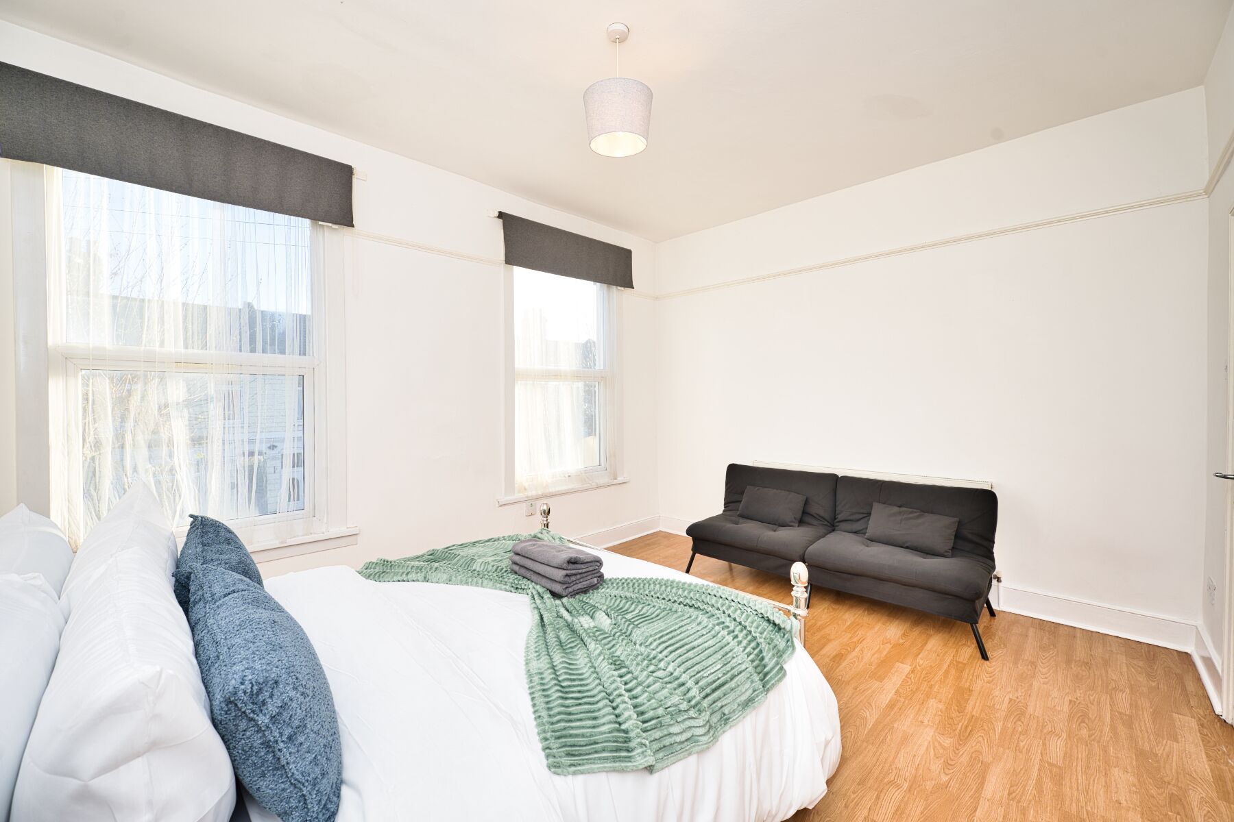 Ein geräumiges Schlafzimmer mit einem großen Bett, einer Couch und zwei Fenstern.