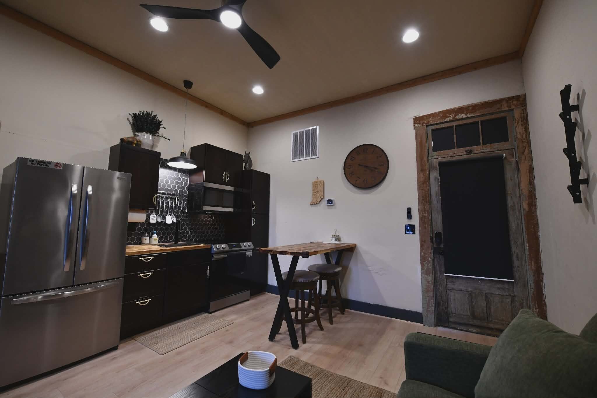 A compact kitchen with modern appliances, a dining area with a wooden table and stools, and a rustic door.
