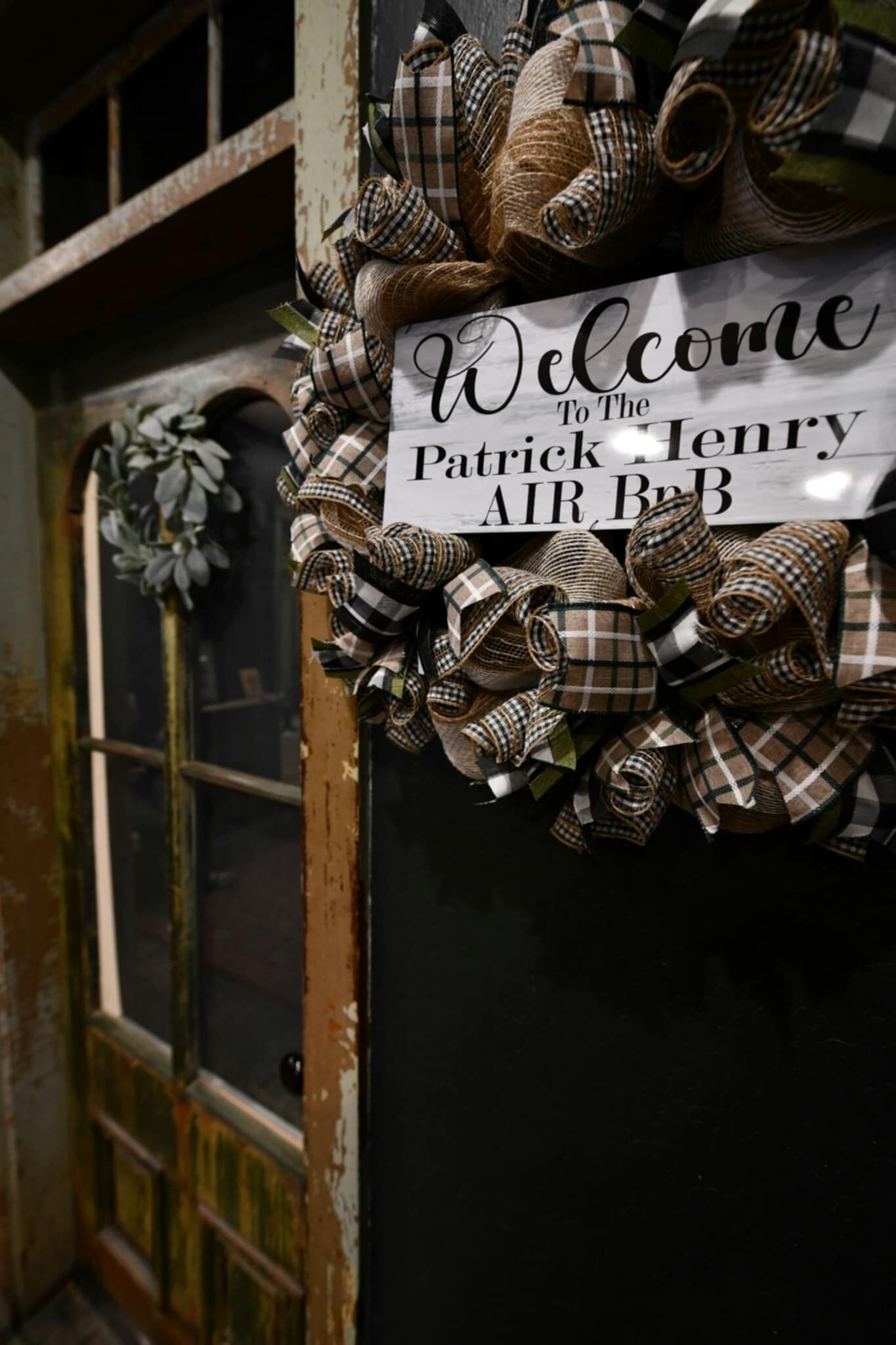 Eine Tür mit einem Schild, auf dem 'Welcome to the Patrick Henry AIR, BrB' steht, umgeben von Jutestoff und Karobögen.