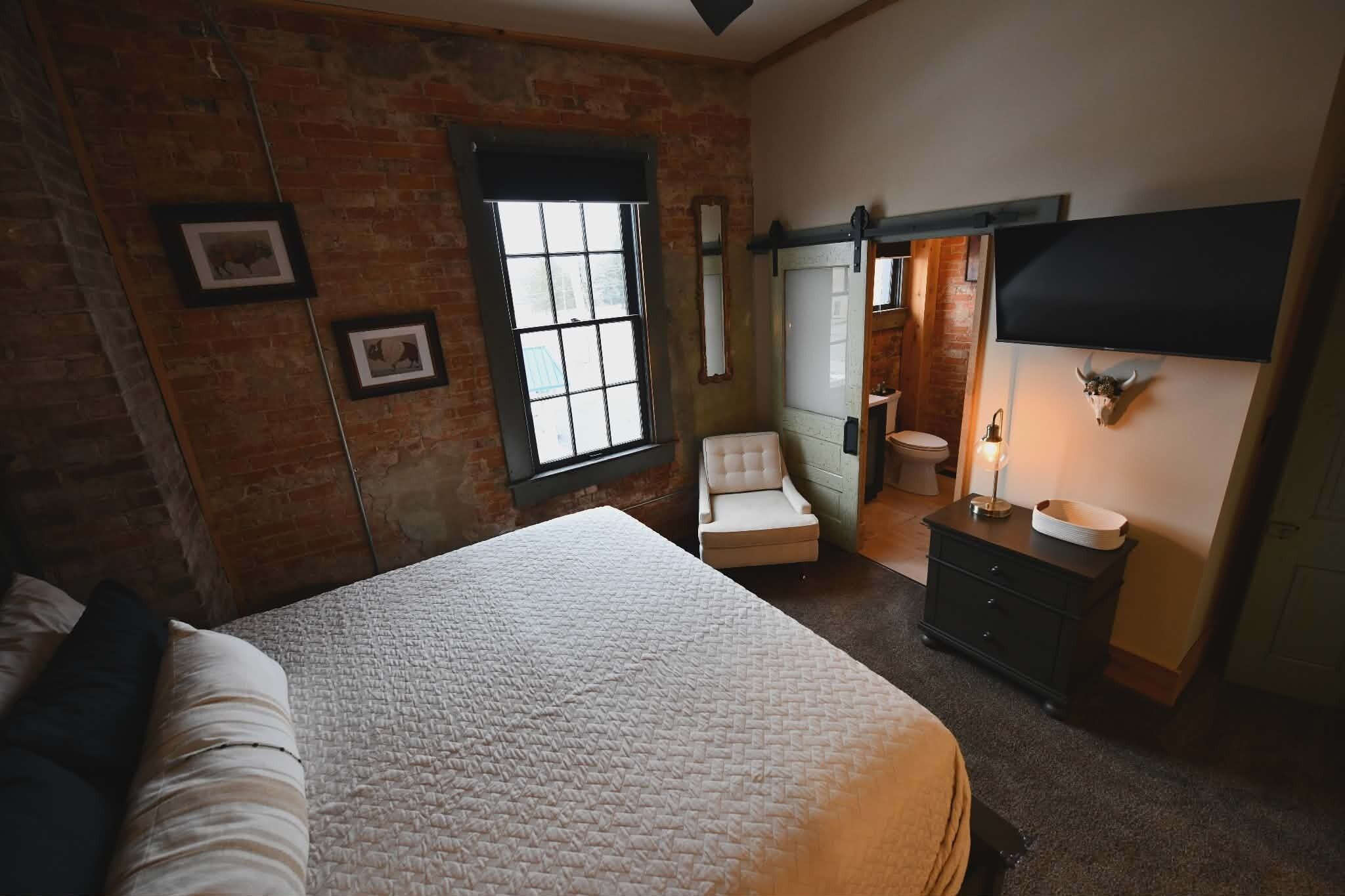 Une chambre à coucher avec un grand lit, une chaise, une commode, un miroir et un téléviseur.
