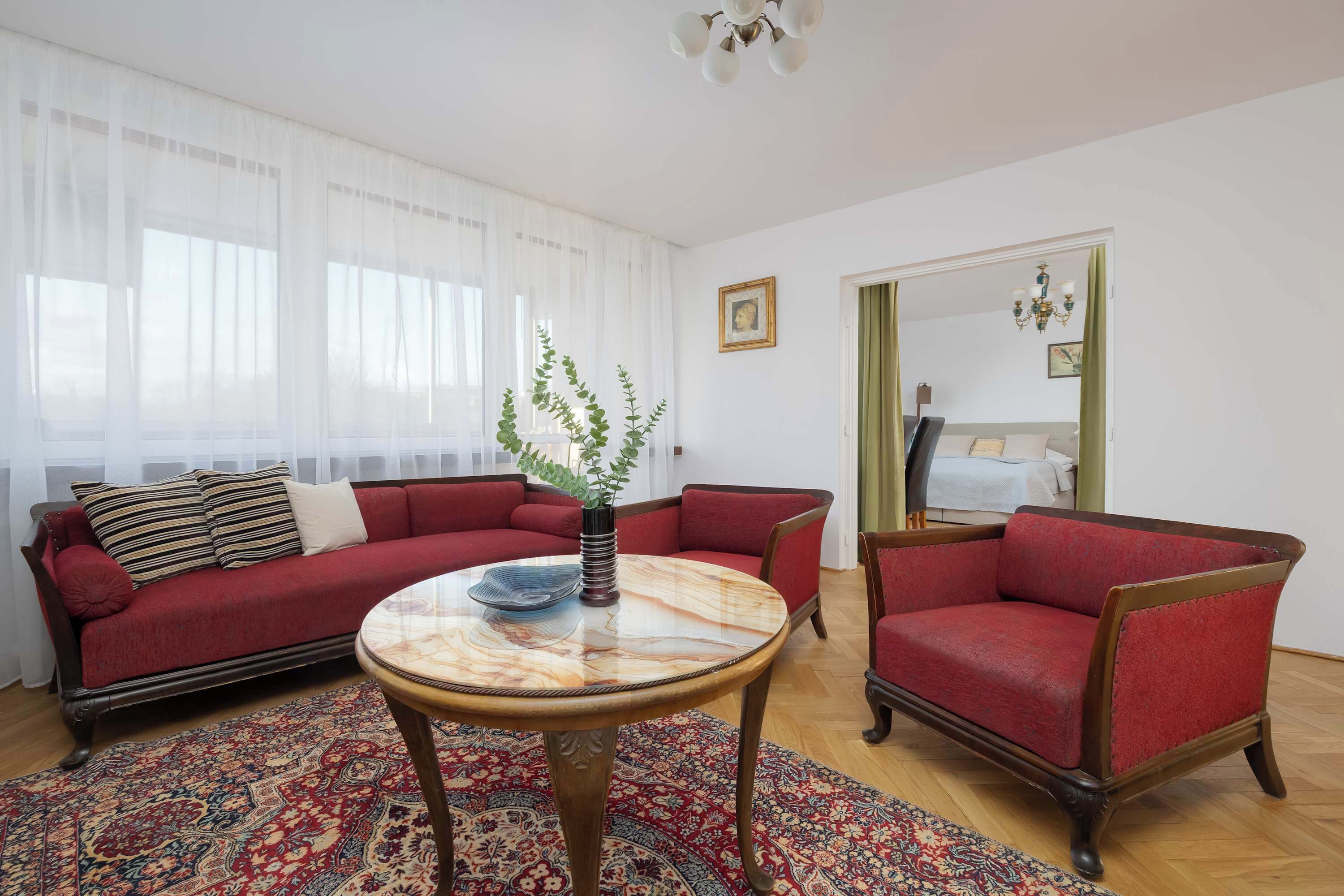 Ein Wohnzimmer mit einer roten Couch, einem runden Holztisch und einem gemusterten Teppich.