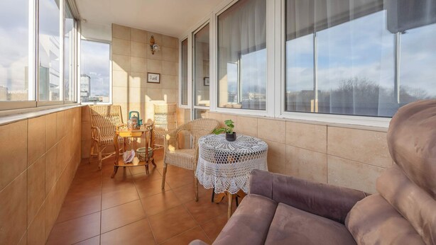 Ein Balkon mit Korbstühlen, einem kleinen runden Tisch mit Pflanze und einer gepolsterten Couch.