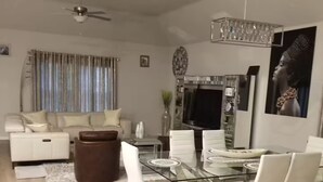A modern living room with a glass dining table, white sofas, and a ceiling fan. - Sweetliving home (Venus)