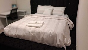 A neatly made bed with a white comforter and pillows, a black headboard, and a small bedside table with a lamp. - Sweetliving home (Venus)
