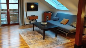 A spacious living room with a wooden floor, a sofa, a coffee table, a TV, and a skylight. - Old Town Apartment Luka (Roding)