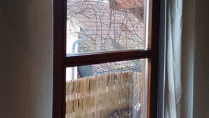 A window with a wooden frame and a view of a building with a brick facade and a metal fence. - Old Town Apartment Luka (Roding)