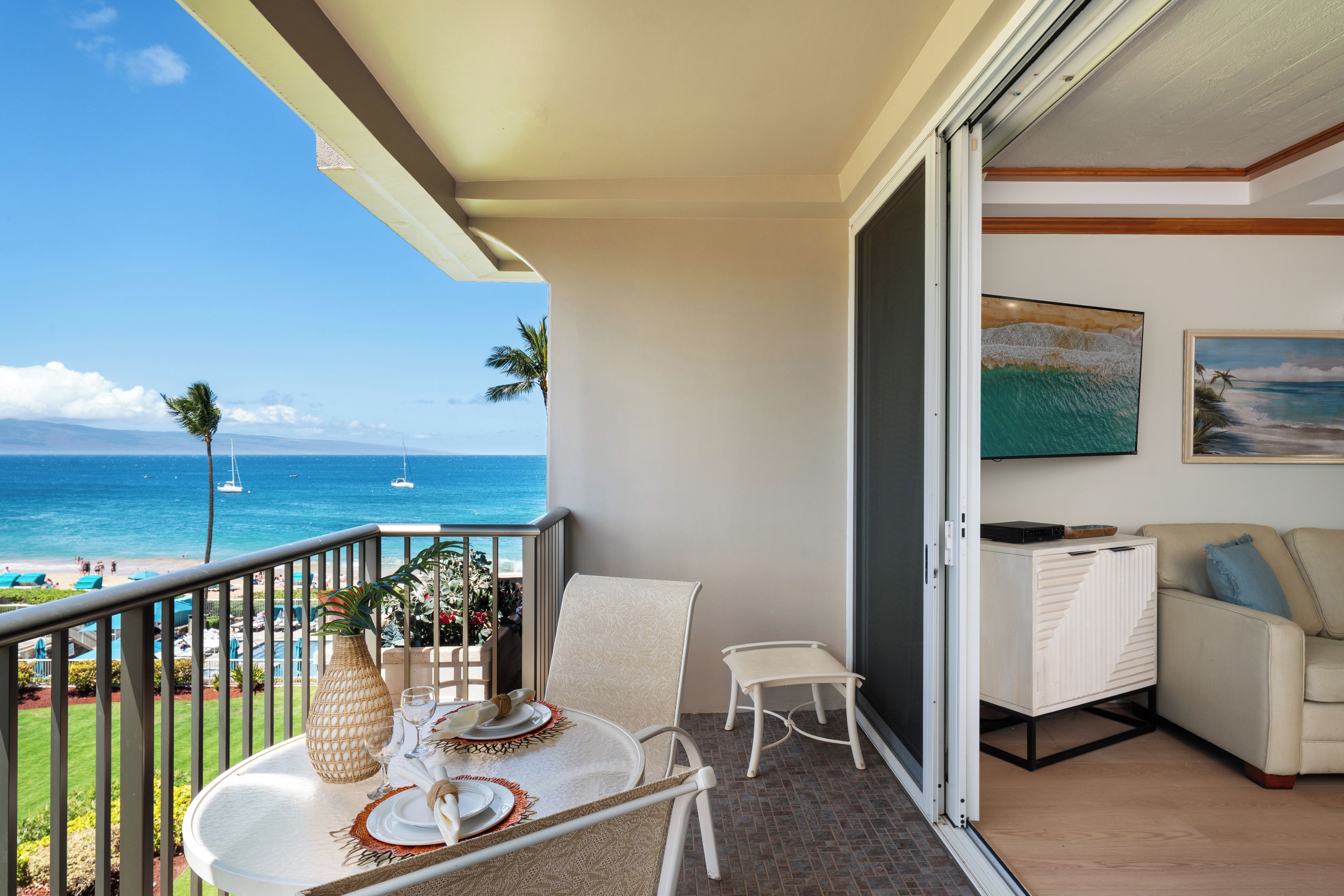 Ein Balkon mit Meerblick, ein Esstisch mit Tellern und einer Vase, eine Couch und ein Schrank.