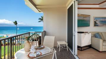 Ein Balkon mit Meerblick, ein Esstisch mit Tellern und einer Vase, eine Couch und ein Schrank.
