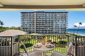 A balcony with a table set for dining, overlooking a large building and a beach.